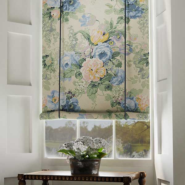 Floral pastel fabric on a Roman blind, complemented by soft cream walls and woven rattan textures for a fresh botanical interior.